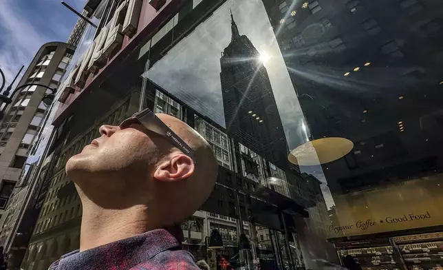 A window reflection of the Empire State building appears behind James Hudson, left, from Long Island, N.Y., as he wears special glasses to view a partial eclipse of the moon covering the sun, Monday April 8, 2024, in New York. (AP Photo/Bebeto Matthews)