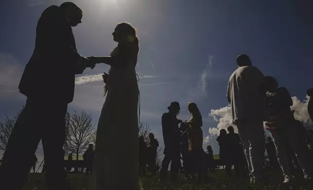 Couples to be wed exchange rings just before totality during a solar eclipse during a mass wedding ceremony at Trenton Community Park, Monday, April 8, 2024, in Trenton, Ohio. (AP Photo/Jon Cherry)
