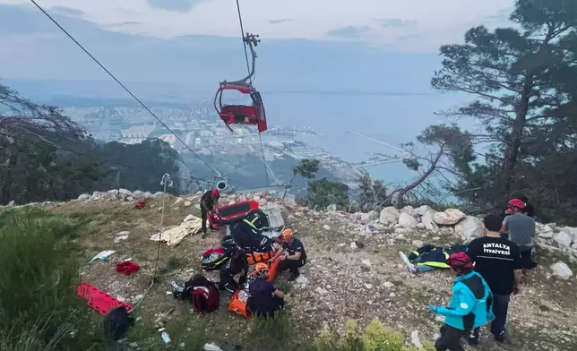 Rescue and emergency team members work with passengers of a cable car transportation system outside Antalya, southern Turkey, Friday, April 12, 2024. At least one person was killed and several injured Friday when a cable car pod in southern Turkey hit a pole and burst open, sending the passengers plummeting to the mountainside below, officials and local media said. Scores of other people were left stranded late into the night after the entire cable car system came to a standstill. (Dia Images via AP)
