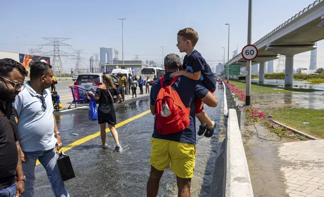 A man carries a child through floodwater caused by heavy rain while waiting for transportation on Sheikh Zayed Road highway in Dubai, United Arab Emirates, Thursday, April 18, 2024. The United Arab Emirates attempted to dry out Thursday from the heaviest rain the desert nation has ever recorded, a deluge that flooded out Dubai International Airport and disrupted flights through the world's busiest airfield for international travel. (AP Photo/Christopher Pike)