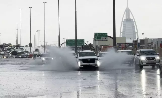 An SUV splashes through standing water on a road with the Burj Al Arab luxury hotel seen in the background in Dubai, United Arab Emirates, Tuesday, April 16, 2024. Heavy rains lashed the United Arab Emirates on Tuesday, flooding out portions of major highways and leaving vehicles abandoned on roadways across Dubai. Meanwhile, the death toll in separate heavy flooding in neighboring Oman rose to 18 with others still missing as the sultanate prepared for the storm. (AP Photo/Jon Gambrell)