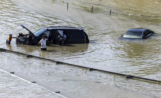 A group of people work to recover an abandoned vehicle taken by floodwater caused by heavy rain in Dubai, United Arab Emirates, Thursday, April 18, 2024. The United Arab Emirates attempted to dry out Thursday from the heaviest rain the desert nation has ever recorded, a deluge that flooded out Dubai International Airport and disrupted flights through the world's busiest airfield for international travel. (AP Photo/Christopher Pike)