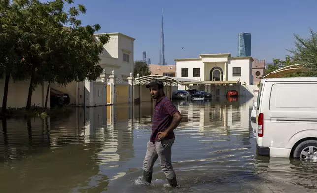 A man walks through standing floodwater caused by heavy rain with the Burj Khalifa, the world's tallest building, seen in Dubai, United Arab Emirates, Thursday, April 18, 2024. The United Arab Emirates attempted to dry out Thursday from the heaviest rain the desert nation has ever recorded, a deluge that flooded out Dubai International Airport and disrupted flights through the world's busiest airfield for international travel. (AP Photo/Christopher Pike)