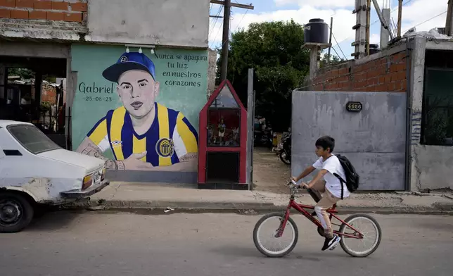 A child rides a bicycle past a mural of Gabriel Ignacio Romero, a resident who was murdered on the sidewalk outside his home the previous year, in Rosario, Argentina, Monday, April 8, 2024. For the past decade, the 1.3 million residents of Rosario have watched warily as presidents and their promises come and go. What endures, they say, is violence. (AP Photo/Natacha Pisarenko)
