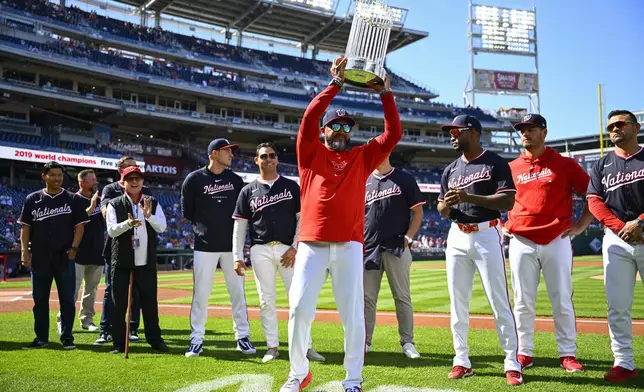 Washington Nationals manager Dave Martinez, center, holds up the 2019 World Series trophy during a pre-game ceremony to celebrate the five year anniversary of the Nationals win over the Houston Astros in the 2019 World Series before a baseball game between the two teams at Nationals Park, Saturday, April 20, 2024, in Washington. (AP Photo/John McDonnell)