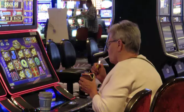 A gambler lights a cigarette at a slot machine in Harrah's casino in Atlantic City N.J., on Sept. 29, 2023. On Monday, April 29, 2024, Atlantic City's main casino workers union asked a judge to let it intervene in that lawsuit. (AP Photo/Wayne