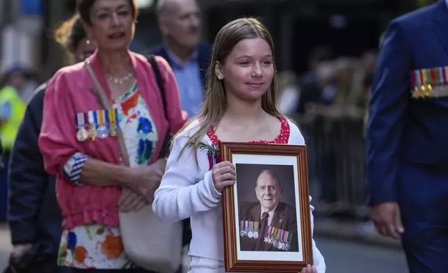 A girl holds a photo as she marches during the Anzac Day parade in central the business district of Sydney, Australia, Thursday, April 25, 2024. (AP Photo/Mark Baker)