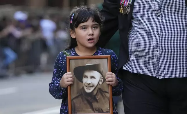 A young girl holds a photo as she marches during the Anzac Day parade in central the business district of Sydney, Australia, Thursday, April 25, 2024. (AP Photo/Mark Baker)