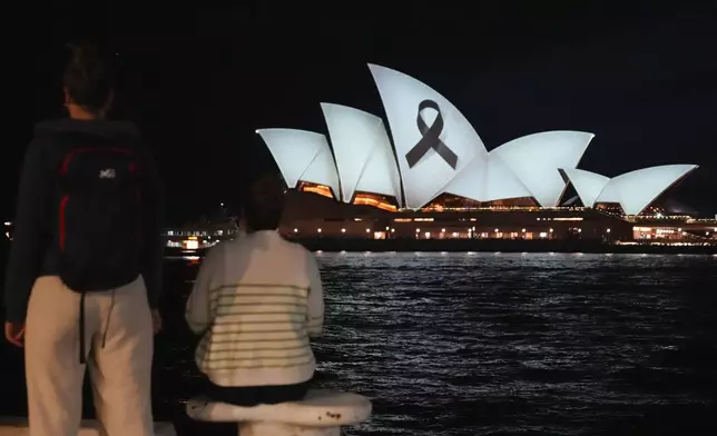 People look as the Sydney Opera House is illuminated with a black ribbon Monday, April 15, 2024, as part of the national day of mourning following the stabbing deaths at a shopping mall in Sydney's East on Saturday. Australian police are examining why a lone assailant who stabbed multiple people to death in a busy Sydney shopping mall and injured more than a dozen others targeted women while avoiding men. (AP Photo/Mark Baker)