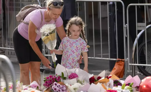 A girl and a woman place flowers as a tribute near a crime scene at Bondi Junction in Sydney, Monday, April 15, 2024, after several people were stabbed to death at a shopping on April 13. Australian police are examining why a lone assailant who stabbed several people to death in a busy Sydney shopping mall and injured more than a dozen others targeted women while avoiding men. (AP Photo/Mark Baker)