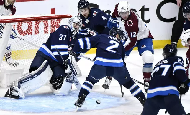 Winnipeg Jets goaltender Connor Hellebuyck (37) watches the puck as Colorado Avalanche right wing Brandon Duhaime (12) looks for a rebound during the second period in Game 1 of an NHL hockey Stanley Cup first-round playoff series in Winnipeg, Manitoba, Sunday April 21, 2024. (Fred Greenslade/The Canadian Press via AP)