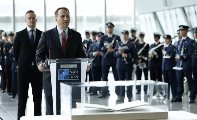 Poland's Foreign Minister Radoslaw Sikorski, center, addresses the audience as he stands behind the original Washington Treaty during a ceremony to mark the 75th anniversary of NATO at NATO headquarters in Brussels, Thursday, April 4, 2024. NATO marked on Thursday 75 years of collective defense across Europe and North America, with its top diplomats vowing to stay the course in Ukraine as better armed Russian troops assert control on the battlefield. (AP Photo/Geert Vanden Wijngaert)