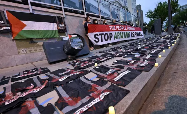 Demonstrators hold a sign while press vest lay on the ground covered in red paint during a pro-Palestinian protest over the Israel-Hamas war at the White House Correspondents' Association Dinner, Saturday April 27, 2024, in Washington. (AP Photo/Terrance Williams)