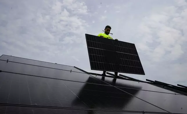 FILE - Nicholas Hartnett, owner of Pure Power Solar, holds a panel as his company installs a solar array on the roof of a home in Frankfort, Ky., July 17, 2023. (AP Photo/Michael Conroy, File)