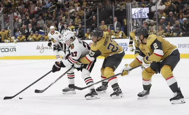 Chicago Blackhawks left wing Lukas Reichel (27) skates past Vegas Golden Knights defensemen Alec Martinez (23) and Zach Whitecloud (2) during the first period of an NHL hockey game Tuesday, April 16, 2024, in Las Vegas. (AP Photo/Ian Maule)