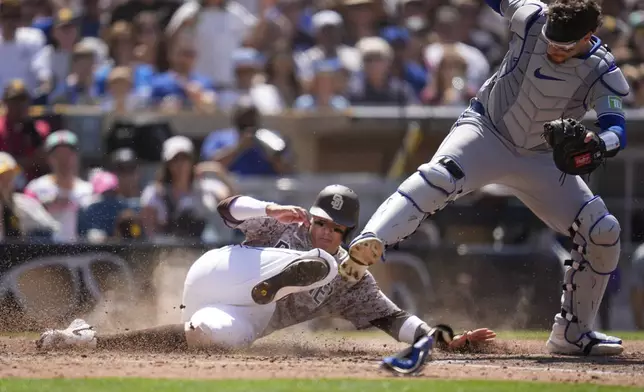 San Diego Padres' Manny Machado, left, slides in late to home after Jackson Merrill grounded into a force out as Toronto Blue Jays catcher Danny Jansen is knocked off the base, right, during the sixth inning of a baseball game, Sunday, April 21, 2024, in San Diego. (AP Photo/Gregory Bull)