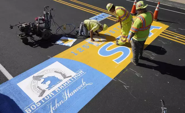 FILE - Painter Will Belezos, of Holbrook, Mass., left, uses a stencil, Wednesday, Oct 6, 2021, while working to complete the start line for the 125th edition of the Boston Marathon, in Hopkinton, Mass. Once a year for the last 100 years, Hopkinton becomes the center of the running world, thanks to a quirk of geography and history that made it the starting line for the world's oldest and most prestigious annual marathon. (AP Photo/Steven Senne, File)