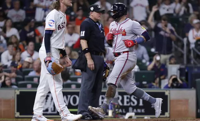 Atlanta Braves runner Adam Duvall, right, scores in front of umpire Tony Randazzo, center, and Houston Astros pitcher Josh Hader on an RBI single by teammate Orlando Arcia during the ninth inning of a baseball game Monday, April 15, 2024, in Houston. (AP Photo/Michael Wyke)