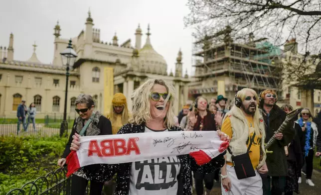 A woman holds an ABBA scarf, during a silent disco event outside the Brighton Dome, in Brighton, England, Saturday, April 6, 2024. Fans are celebrating 50 years since ABBA won its first big battle with “Waterloo.” A half century ago on Saturday, April 6, the Swedish quartet triumphed at the 1974 Eurovision Song Contest with the peppy love song. (AP Photo/Alberto Pezzali)