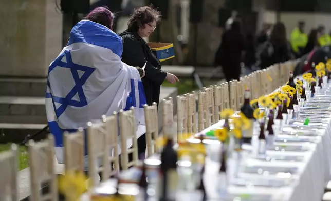 Two women, one of them wrapped in an Israeli flag, help to set the “The Empty Seder Table’ with 133 chairs and place settings, representing the absence of the hostages kidnapped by Hamas militants from Israel and held in Gaza, in front of Downing Street in London, Wednesday, April 17, 2024. (AP Photo/Alastair Grant)