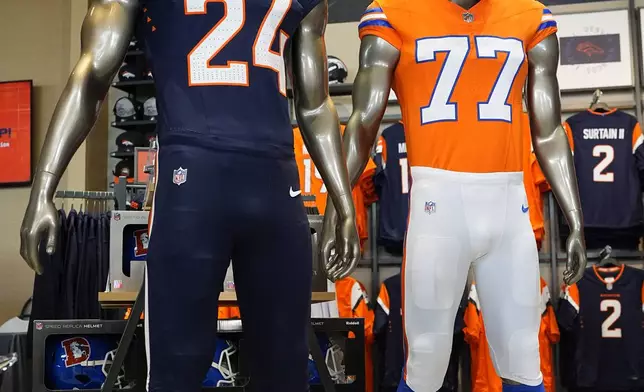 Two of the four new uniforms that the Denver Broncos NFL football team will wear starting in the upcoming season are on display during a news conference at Empower Field at Mile High, Monday, April 22, 2024, in Denver. The update is the first major change to the team's uniforms since 1997. (AP Photo/David Zalubowski)