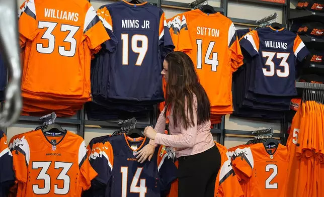 An employee looks at two of the four new uniforms that the Denver Broncos NFL football team will wear starting in the upcoming season during a news conference at Empower Field at Mile High, Monday, April 22, 2024, in Denver. The update is the first major change to the team's uniforms since 1997. (AP Photo/David Zalubowski)