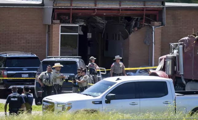 Law enforcement personnel work at the scene after a stolen 18-wheeler crashed into a Texas Department of Public Safety office on US-290 in Brenham, Texas on Friday, April 12, 2024. The driver of a stolen semitrailer intentionally rammed it into the Texas public safety office in a rural town west of Houston on Friday, injuring multiple people, according to a state lawmaker. (Meredith Seaver /College Station Eagle via AP)