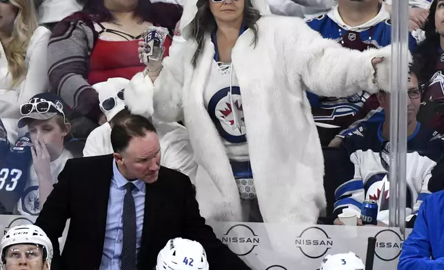 CORRECTS TO COLORADO AVALANCHE ASSISTANT COACH NOLAN PRATT NOT HEAD COACH JARED BEDNAR - A Winnipeg Jets fan, upper center, dances in a polar bear outfit behind Colorado Avalanche assistant coach Nolan Pratt, center left, during the second period in Game 1 of an NHL hockey Stanley Cup first-round playoff series in Winnipeg, Manitoba, Sunday April 21, 2024. (Fred Greenslade/The Canadian Press via AP)