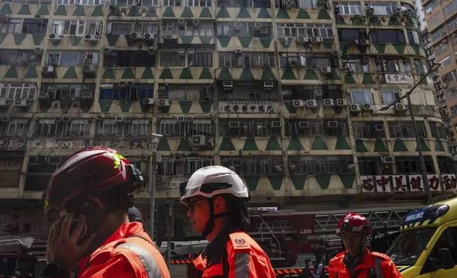 CORRECTS TO AMBULANCE WORKERS INSTEAD OF FIREFIGHTERS - Ambulance workers walk past a building called New Lucky House where a fire started in Hong Kong, Wednesday, April 10, 2024. (AP Photo/Louise Delmotte)