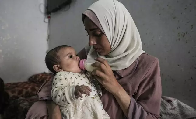 CORRECTS LOCATION - Rola Saqer feeds her baby Masa Mohammad Zaqout at her parents' home in the neighborhood of Zawaida, central Gaza, Thursday, April 4, 2024. Zaqout was born Oct. 7, the day the Israel- Hamas war erupted. Mothers who gave birth that day fret that their 6-month-old babies have known nothing but brutal war, characterized by a lack of baby food, unsanitary shelter conditions and the crashing of airstrikes. (AP Photo/Abdel Kareem Hana)