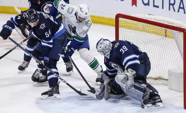 Winnipeg Jets goaltender Laurent Brossoit (39) makes a save against Vancouver Canucks' Pius Suter (24) as Dylan Samberg (54) defends during the third period of an NHL hockey game Thursday, April 18, 2024, in Winnipeg, Manitoba. (John Woods/The Canadian Press via AP)
