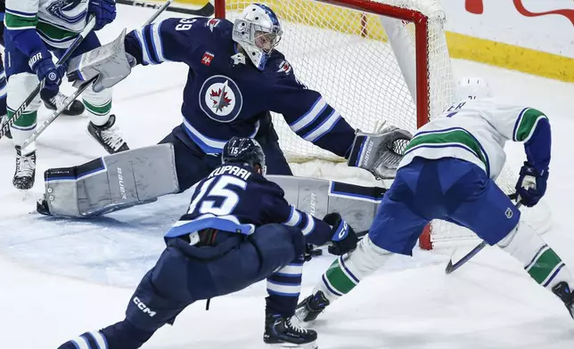 Winnipeg Jets goaltender Laurent Brossoit (39) makes a save against Vancouver Canucks' Pius Suter (24) as Rasmus Kupari (15) defends during the third period of an NHL hockey game Thursday, April 18, 2024, in Winnipeg, Manitoba. (John Woods/The Canadian Press via AP)