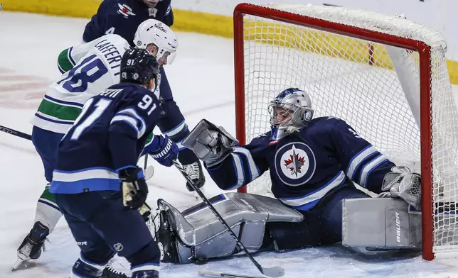 A stick-less Winnipeg Jets goaltender Laurent Brossoit (39) stops a shot as Vancouver Canucks' Sam Lafferty (18) looks for the puck and Cole Perfetti (91) and Neal Pionk (4) defend during the third period of an NHL hockey game Thursday, April 18, 2024, in Winnipeg, Manitoba. (John Woods/The Canadian Press via AP)