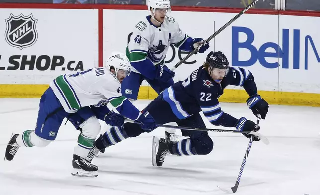 Winnipeg Jets' Mason Appleton (22) reaches out for the pass as Vancouver Canucks' Conor Garland (8) and Elias Pettersson (40) defend during the third period of an NHL hockey game Thursday, April 18, 2024, in Winnipeg, Manitoba. (John Woods/The Canadian Press via AP)