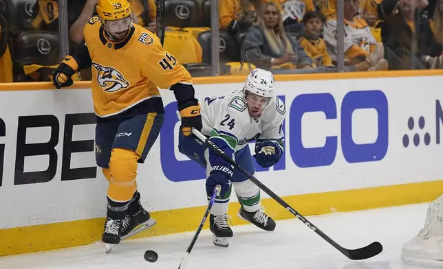 Vancouver Canucks center Pius Suter (24) reaches for the puck past Nashville Predators defenseman Alexandre Carrier (45) during the first period in Game 3 of an NHL hockey Stanley Cup first-round playoff series Friday, April 26, 2024, in Nashville, Tenn. (AP Photo/George Walker IV)