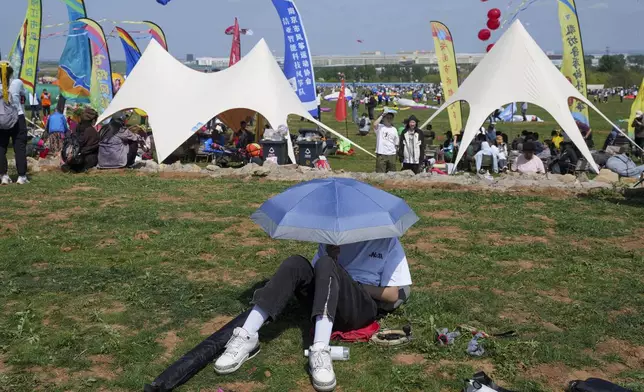 A visitor rests in the shade of an umbrella during the 41st International Kite Festival in Weifang, Shandong Province of China, Saturday, April 20, 2024. (AP Photo/Tatan Syuflana)