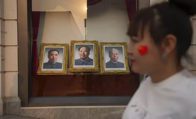 A woman walks past portraits of late Chinese leaders including Mao Zedong at the Wangfujing Shopping street in Beijing, China, Thursday, April 11, 2024. (AP Photo/Tatan Syuflana)