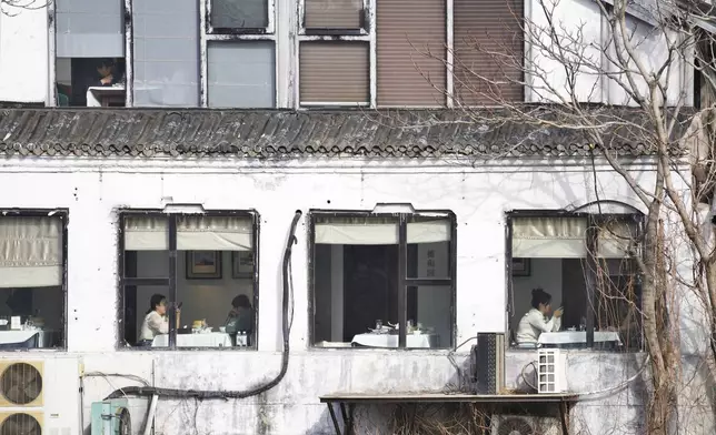 People enjoy their meals at a restaurant are seen through windows near the Forbidden City in Beijing, China, Saturday, March 16, 2024. (AP Photo/Tatan Syuflana)