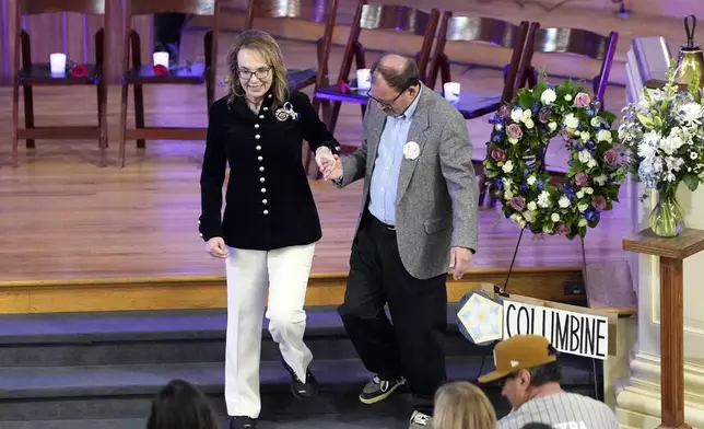 Former Arizona Rep. Gabby Giffords is helped off the stage by Tom Mauser, who is wearing his son's shoes during a vigil remembering the 25th anniversary of the Columbine High School mass shooting, Friday, April 19, 2024, in Denver. Daniel Mauser was killed during the Columbine shooting. (AP Photo/Jack Dempsey)