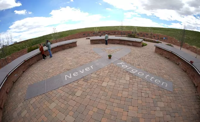In this photograph taken through a fisheye lens, people visit the Columbine Memorial, Wednesday, April 17, 2024, in Littleton, Colo. Trauma still shadows the survivors of the horrific Columbine High School shooting as the attack's 25th anniversary approaches. (AP Photo/David Zalubowski)