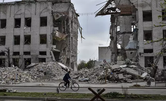 FILE - A local woman rides a bicycle on April 18, 2024, in front of a building destroyed by a Russian airstrike in the frontline town of Orikhiv, Ukraine. House Speaker Mike Johnson, R-La., putting his job on the line, relied on Democratic support this week to bring to the House floor a series of votes on $95 billion in foreign aid for Ukraine, Israel and other U.S. allies. Since President Joe Biden made the funding request in October, the Republican-controlled House has always loomed as the largest obstacle to final passage. (AP Photo/Andriy Andriyenko)