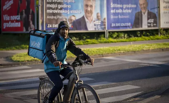 A delivery man rides a bicycle in front of election posters in Zagreb, Croatia, Sunday, April 14, 2024. Croatia this week holds an early parliamentary election following a campaign that was marked by heated exchanges between the country's two top officials, creating a political crisis in the Balkan country, a European Union and NATO member state. (AP Photo/Darko Bandic)