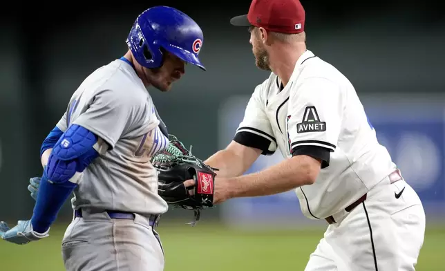 Chicago Cubs' Ian Happ, left, is tagged out by Arizona Diamondbacks pitcher Merrill Kelly on a ground out during the fifth inning of a baseball game, Monday, April 15, 2024, in Phoenix. (AP Photo/Matt York)