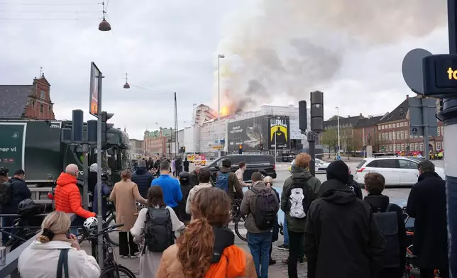 People watch as fire and smoke rise out of the Old Stock Exchange, Boersen, in Copenhagen, Denmark, Tuesday, April 16, 2024. (Emil Helms/Ritzau Scanpix via AP)