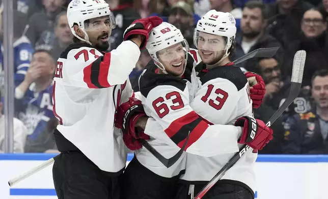 New Jersey Devils left wing Jesper Bratt (63) celebrates his goal against the Toronto Maple Leafs with Jonas Siegenthaler (71) and Nico Hischier (13) during the third period of an NHL hockey game Thursday, April 11, 2024, in Toronto. (Nathan Denette/The Canadian Press via AP)