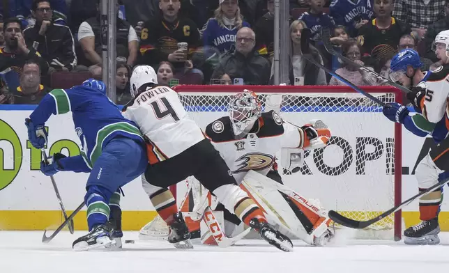 Vancouver Canucks' Brock Boeser, left, scores against Anaheim Ducks goalie Lukas Dostal while being checked by Cam Fowler (4) during the first period of an NHL hockey game Sunday, March 31, 2024, in Vancouver, British Columbia. (Darryl Dyck/The Canadian Press via AP)
