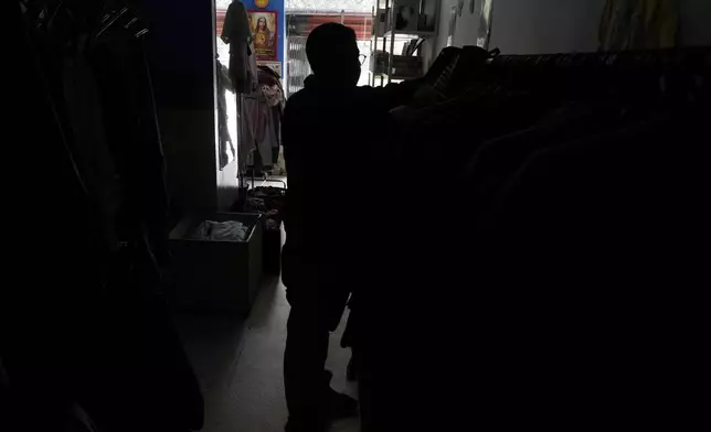 A customer shops for clothes in a store without electricity due to a programed power cut ordered by the ministry of energy, in Quito, Ecuador, Tuesday, April 16, 2024. Ecuador faces electricity rationing due to a prolonged drought and high temperatures that have reduced flows to the main hydroelectric plants. (AP Photo/Dolores Ochoa)