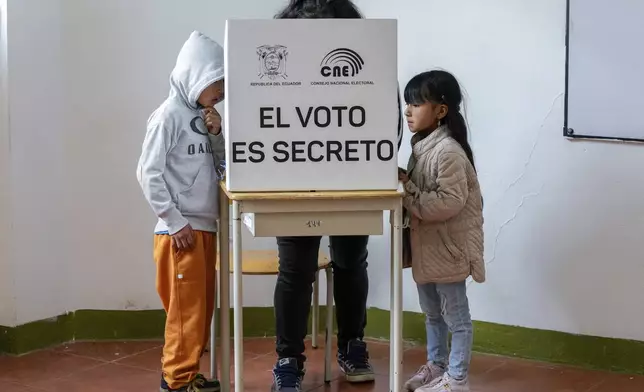 Children stand by a voter marking questions on the ballot of a referendum proposed by President Daniel Noboa to endorse new security measures aimed at crack down on criminal gangs fueling escalating violence in Quito, Ecuador, Sunday, April 21, 2024. (AP Photo/Dolores Ochoa)