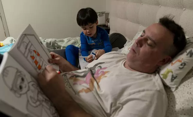 Scott Quinn and his 4-year-old son, Ethan, work on coloring books in a bed in Concord, Calif., Wednesday, Nov. 1, 2023. Ethan's parents are among those who have opted for a private daycare instead of a free “transitional kindergarten.” Quinn said he has been discouraged to see Ethan — one of the oldest kids in his daycare class — pick up the behavior of kids who are several years younger than him. “In retrospect, it would have been better to send him to school to be around kids his age and older,” he said. (AP Photo/Jae C. Hong)