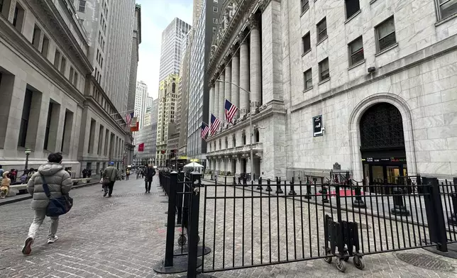 People pass the New York Stock Exchange, right, on Wednesday, April 17, 2024 in New York. Global shares are trading mixed after most U.S. stocks slipped on firmer expectations that the Fed is committed to its current rate practices.(AP Photo/Peter Morgan)